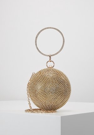 Ronde gouden clutch met strasspatroon, gouden kettingriem en een grote, met strass bezette cirkelvormige polsband op een witte sokkel.