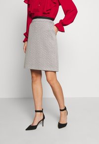 Harmaa teksturoidulla A-linjaisella hameella, jossa on musta vyötärö, yhdistettynä punaiseen puseroon ja mustiin nilkkaketjukenkiin.