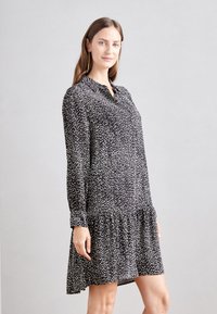 Čierno-biel dress s bodkami, dlhými rukávmi, so zapínaním na gombíky na prednej strane a riaseným lemom. Vyrobené z ľahkej tkaniny s hladkou textúrou.