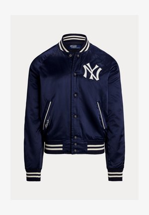 Granatowa satynowa kurtka bomber z białymi paskami na kołnierzu, mankietach i dole, logo New York Yankees na piersi oraz zapinana na guziki z przodu.