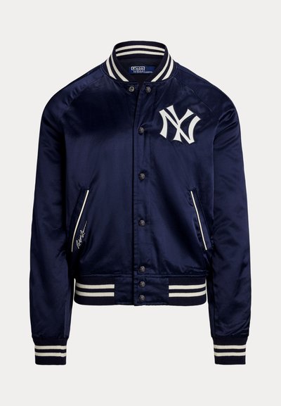 Tengerészkék szatén bomberdzseki fehér csíkos gallérral, mandzsettákkal és szegéllyel, New York Yankees logóval a mellkason, elején gombos rögzítéssel.