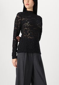 Black lace top with long sleeves, high collar, floral pattern, and sheer texture, paired with loose gray trousers.