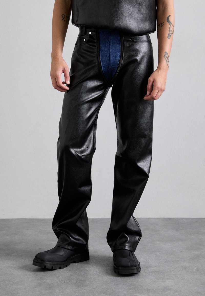 Black leather pants with a blue denim insert at the front, featuring a relaxed fit, subtle sheen, and a zip closure. Chunky black boots.