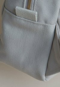 Ljusgrå tygryggsäck med en texturerad yta, dragkedjestängning och en utvändig ficka med en platt flik för enkel åtkomst.