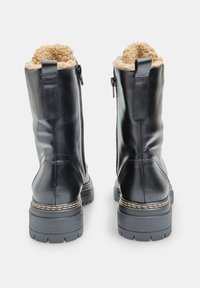 Botas de tobillo de cuero negro con forro de pelaje sintético, que cuentan con cremalleras laterales, suelas de goma resistentes y costuras de contraste a lo largo de la suela.