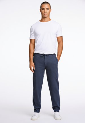 Camiseta blanca de cuello redondo combinada con pantalones sueltos de lino azul marino. El modelo lleva zapatillas blancas. Textura suave, diseño casual y cintura con cordón.
