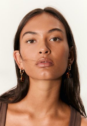 Boucles d'oreilles en or avec des accents en écaille de tortue. Texture de surface lisse. Gros plan avec un ton de peau naturel et un éclairage doux.