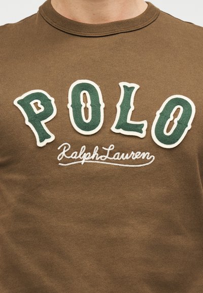 Καφέ βαμβακερό μπλουζάκι με ριμπ λαιμόκοψη, με μεγάλα πράσινα κεντημένα γράμματα "POLO" και το λευκό κείμενο "RalphLauren" από κάτω.