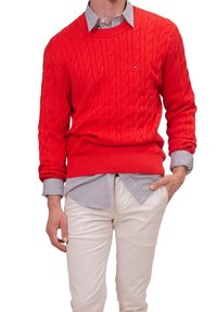 Pull rouge en tricot torsadé en coton, porté par-dessus une chemise rayée. Comprend des poignets et un ourlet côtelés, associé à un pantalon de couleur claire.