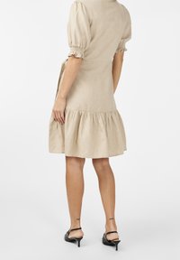 Beiges Leinenkleid mit Puffärmeln, rüschsaum und Bindeband in der Taille. Tragen mit schwarzen Absatzsandalen.