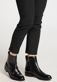 Stivali ankle in pelle nera con un design classico, punta affusolata, zip laterale e tacco basso a blocco. Texture liscia e silhouette elegante.