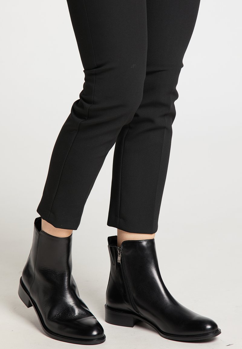 Stivali ankle in pelle nera con un design classico, punta affusolata, zip laterale e tacco basso a blocco. Texture liscia e silhouette elegante.