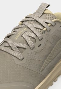 Μπεζ αθλητικό παπούτσι με κορδόνια, υφασμάτινη υφή, επενδεδυμένο γιακά και ετικέτα στη γλώσσα με την επιγραφή "ALTRA LONE PEAK 38".