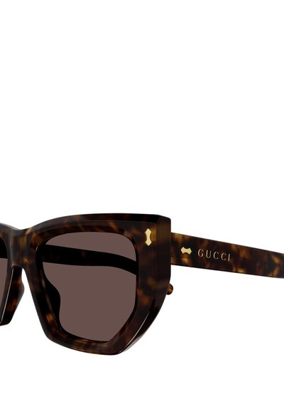 Occhiali da sole tartarugati con una montatura geometrica spessa, lenti marroni scure e dettagli in tono oro sulle tempie che mostrano il logo Gucci.