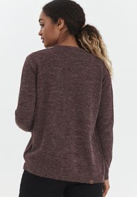 Pull en maille bordeaux avec un col rond, des manches longues et une coupe ample. Présente une surface texturée et une petite étiquette logo près de l'ourlet.