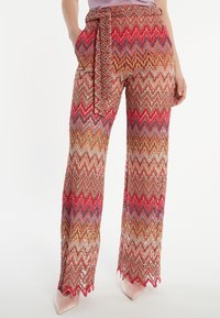 Pantalons larges à motifs en zigzag comprenant des nuances de rouge, marron et bleu. Comprend une ceinture assortie et des poches latérales.