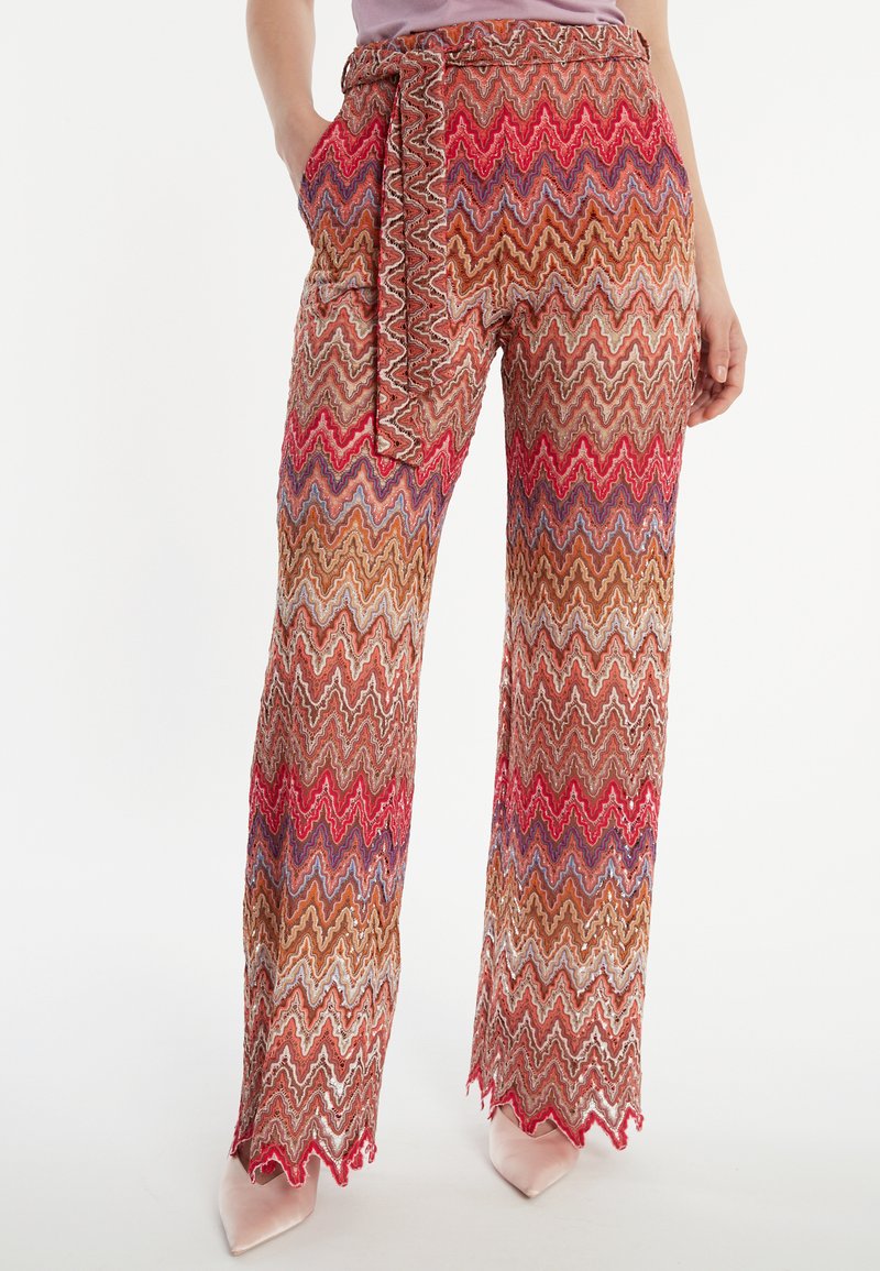 Pantalons larges à motifs en zigzag comprenant des nuances de rouge, marron et bleu. Comprend une ceinture assortie et des poches latérales.