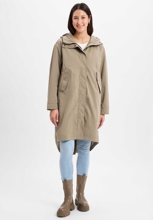 Khaki lichtgewicht regenjack met een capuchon, twee zijzakken en een langere achterzoom, gecombineerd met lichtblauwe skinny jeans en bruine enkelbooties.