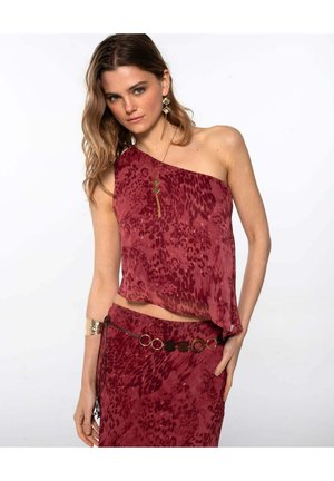 Mujer vestida con una blusa sin mangas roja con un patrón, un hombro al descubierto, falda a juego, joyería dorada y un cinturón de eslabones.