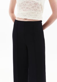 Svarta vida byxor i mjukt tyg, med en skräddarsydd silhuett och rena linjer, parat med en kortärmad spetsblus i off-white.