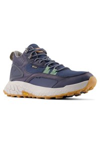 Zapatilla de trail running en color azul marino y verde, fabricada en Gore-Tex, con una gruesa entresuela blanca, suela Vibram de goma y sistema de cierre con cordones.