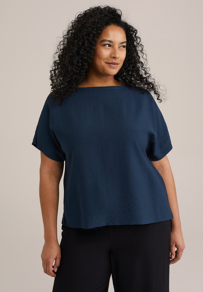 Top de manga corta azul marino con forma cuadrada y un escote amplio, fabricado en un tejido ligero con una sutil textura. Combinado con pantalones negros.