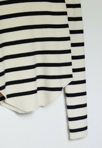 Pull rayé en crème et noir, avec une texture côtelée, à manches longues et un ourlet arrondi, présentant des rayures épaisses et fines qui alternent.
