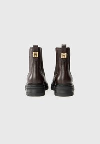 Bruine leren enkellaarzen met een gestructureerde afwerking, elastische zijkanten en een gouden logo-accent op de hiel, voorzien van een zwarte rubberen zool.