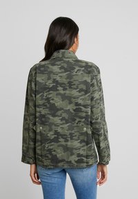Camo jacket in dark green and gray tones; features a classic collar, button details, and a relaxed fit with long sleeves.