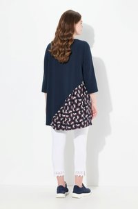 Marinblå tunika med ett mönstrat underdel som har en geometrisk design. Tillsammans med vita leggings med spetsdetaljer och mörka sneakers.