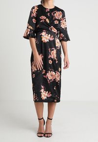 Černé květinové šaty s krátkými volánkovými rukávy, detailním zkroucením vpředu a délkou po kolena. Mají vzory oranžových a růžových květin.