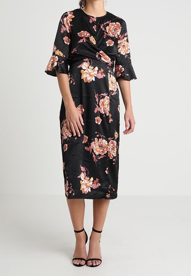 Černé květinové šaty s krátkými volánkovými rukávy, detailním zkroucením vpředu a délkou po kolena. Mají vzory oranžových a růžových květin.