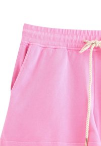 Pantaloni della tuta rosa chiaro con una texture morbida, dotati di un elastico in vita di colore crema e una tasca laterale.