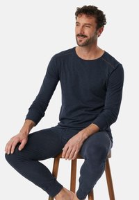 Tmavě modrá košile s dlouhým rukávem a odpovídající kalhoty z měkké látky; mají slim fit a jemné akcentové prošívání na ramenou.