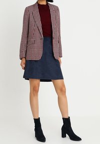 Bleiseri punaisella ja valkoisella houndstooth-kuviolla, yhdistettynä viininpunaisiin yläosiin ja tummansinisiin mokkasinahkahameisiin. Mustat nilkkasaappaat täydentävät ilmeen.