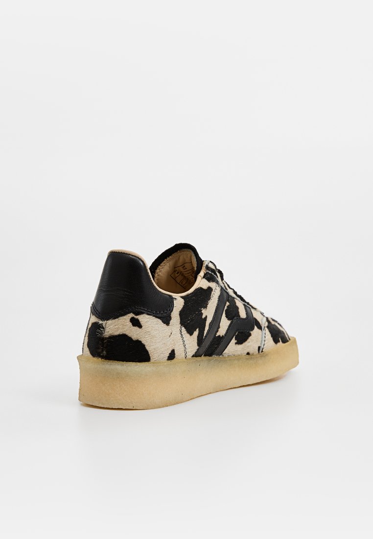 Schwarze und weiße Kuhfell-Leder-Sneaker mit strukturiertem Finish, schwarzen Akzenten und einer beige Gummisohle. Klassisches Low-Top-Design.