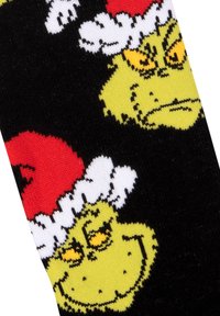 Calzini neri con facce di Grinch in stile cartone animato, pelle gialla, cappelli di Babbo Natale rossi e dettagli in soffice bianco. Design a maglia dettagliato con colori vivaci.