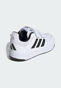 Biela športová obuv s páskami na suchý zips, štruktúrovaný syntetický zvršok, čierne akcenty a kontrastné logo troch pruhov na boku.