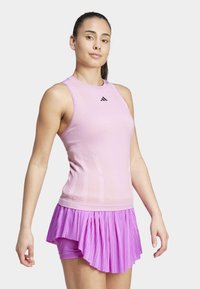 Roze sporttop met geribbelde textuur en aansluitend ontwerp, gecombineerd met een plooirok in paars. Bevat het Adidas-logo op de top.
