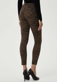 Leggings de estampado de cebra en marrón y negro con un diseño ajustado, de tiro medio y longitud corta, combinados con tacones altos negros.