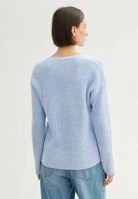 Lichtblauwe gebreide trui met een relaxte pasvorm, geribbelde textuur en brede halslijn, gecombineerd met casual denim jeans.