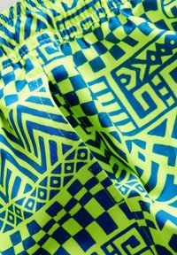 Tissu vert néon avec des motifs géométriques et abstraits bleus. Doté d'une taille élastique et d'une texture douce. Convient pour les vêtements de sport.