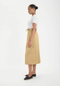 Jupe midi en coton beige avec une taille élastique et un cordon de serrage, associée à une chemise blanche à manches courtes et des espadrilles noires.