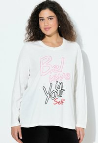 Weißes Langarm-T-Shirt mit Rundhalsausschnitt. Mit mehrfarbigem Text "Glaube an dich selbst" in Pink und Schwarz. Weicher Stoff, lockere Passform.