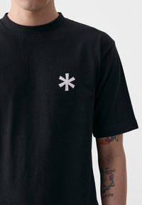 Black cotton t-shirt with a short sleeve design. Features a white asterisk logo on the left chest area. Soft texture, classic fit.