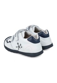 Zapatillas infantiles blancas y azul marino con correas de Velcro, suela de goma texturizada y detalles gráficos en negro en los laterales.