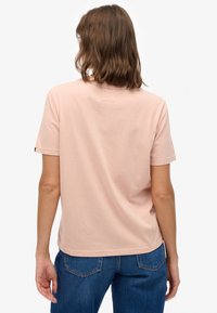 Jasnoróżowy bawełniany t-shirt z krótkimi rękawami i luźnym krojem. Posiada małą metkę marki na lewym rękawie oraz gładkie, jednolite tyły.