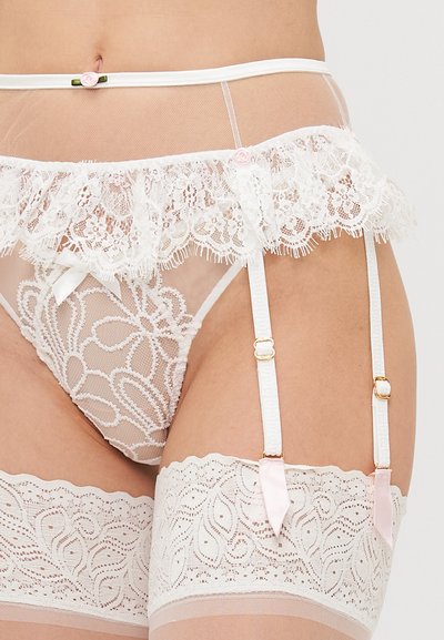 Ce porte-jarretelles en dentelle blanche est orné de volants, d'un motif floral et d'accents en satin. Des jarretelles attachées présentent des finitions en métal doré et des détails en ruban rose.