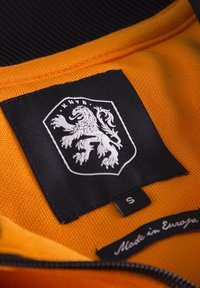 Tessuto arancione con una finitura testurizzata, caratterizzato da un'etichetta nera con un logo di leone bianco e un'etichetta di taglia "S," insieme al testo "Made in Europe."