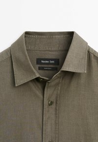 Chemise boutonnée vert olive avec col pointu, un seul bouton visible, et étiquette intérieure portant l'inscription "Massimo Dutti, Fabriqué en Chine".